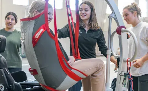 Students help a Maine Adaptive client into a power wheelchair using a lift